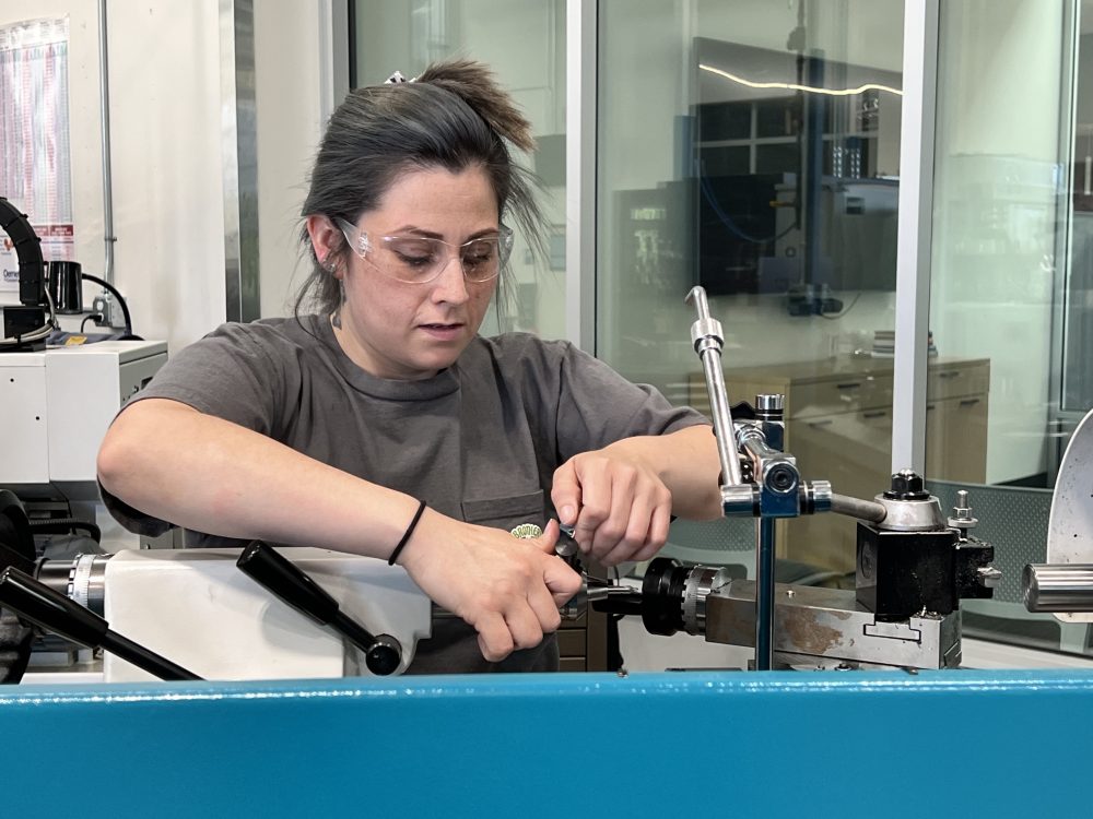 A PCC Career Pathways & STEP student, Lisa, operates a machine in a factory, demonstrating skill and focus in a manufacturing environment.