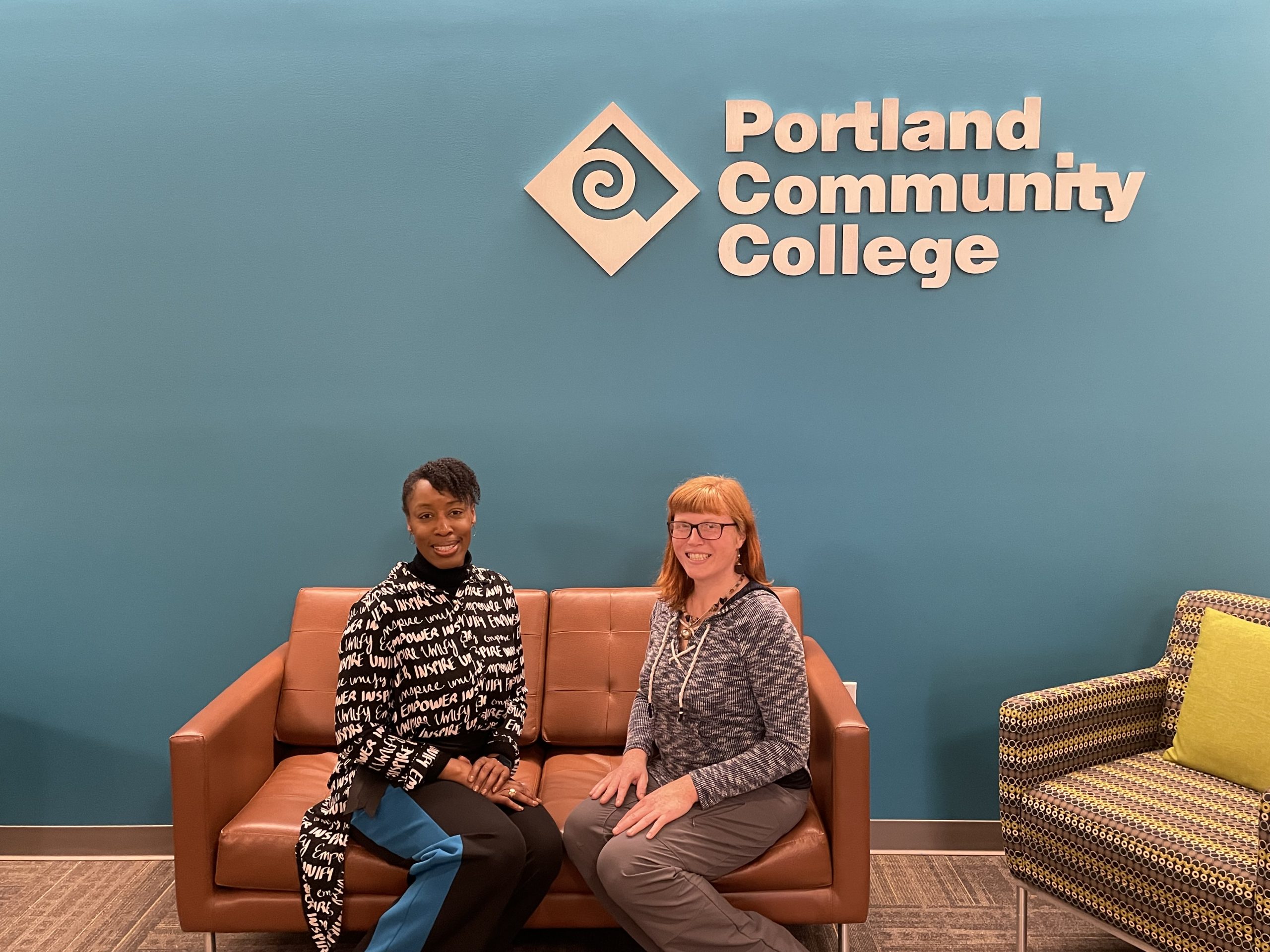 Dr. Adrien Bennings and Carrie Cantrell sitting on a couch and smiling. Behind them is a wall with the PCC logo.
