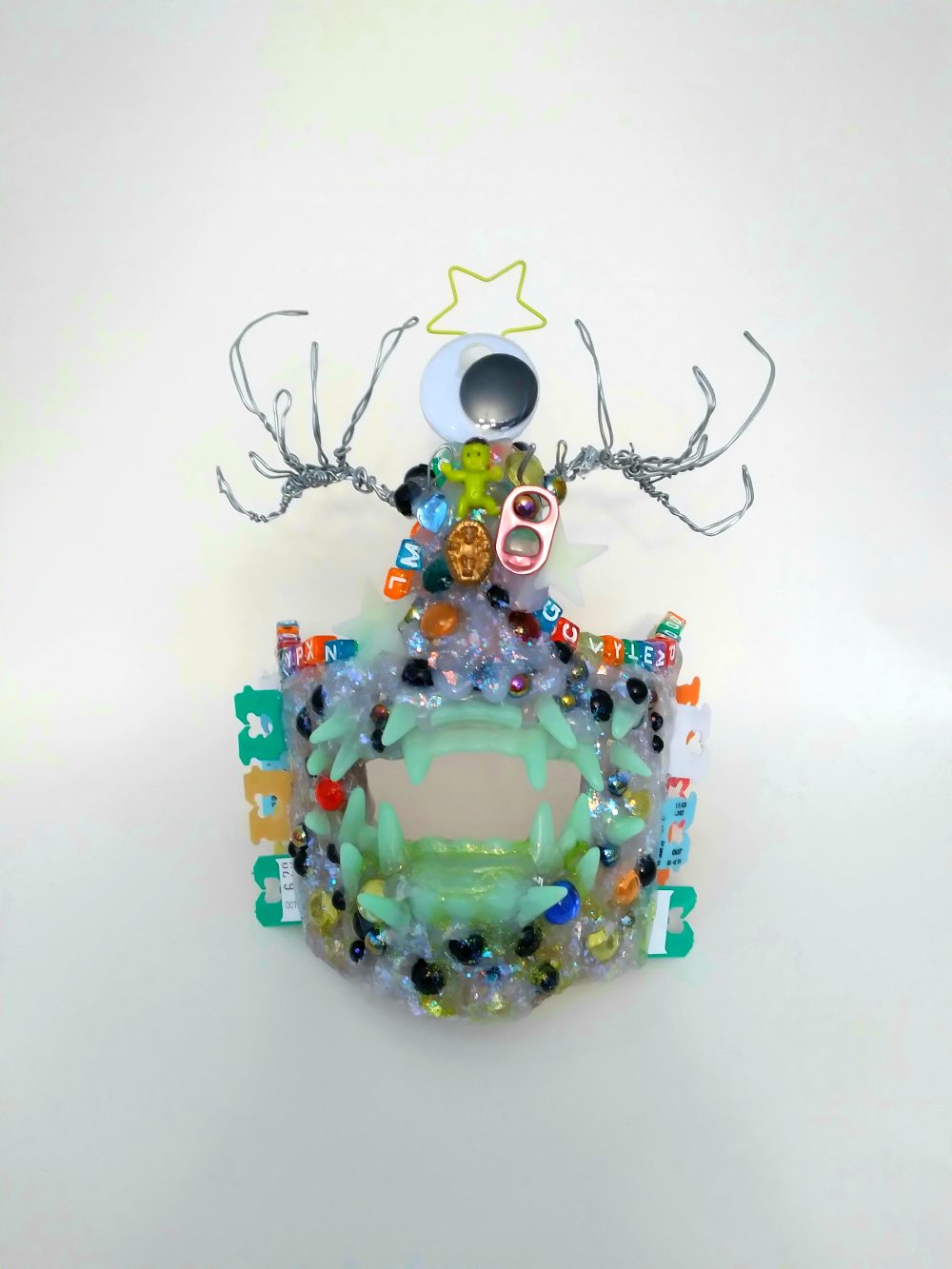 A sculpture of a glittery white monster mask, covered with an assortment of plastic and metal embellishments.