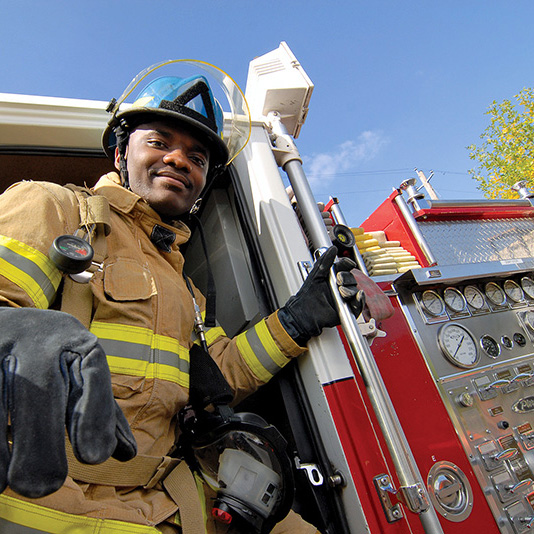 Student in fire protection program wearing protective uniform in front of a fire truck