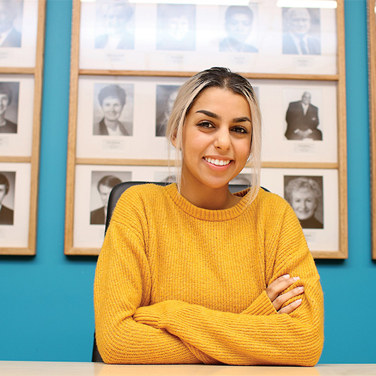 Student sitting at a table on campus smiling into the camera