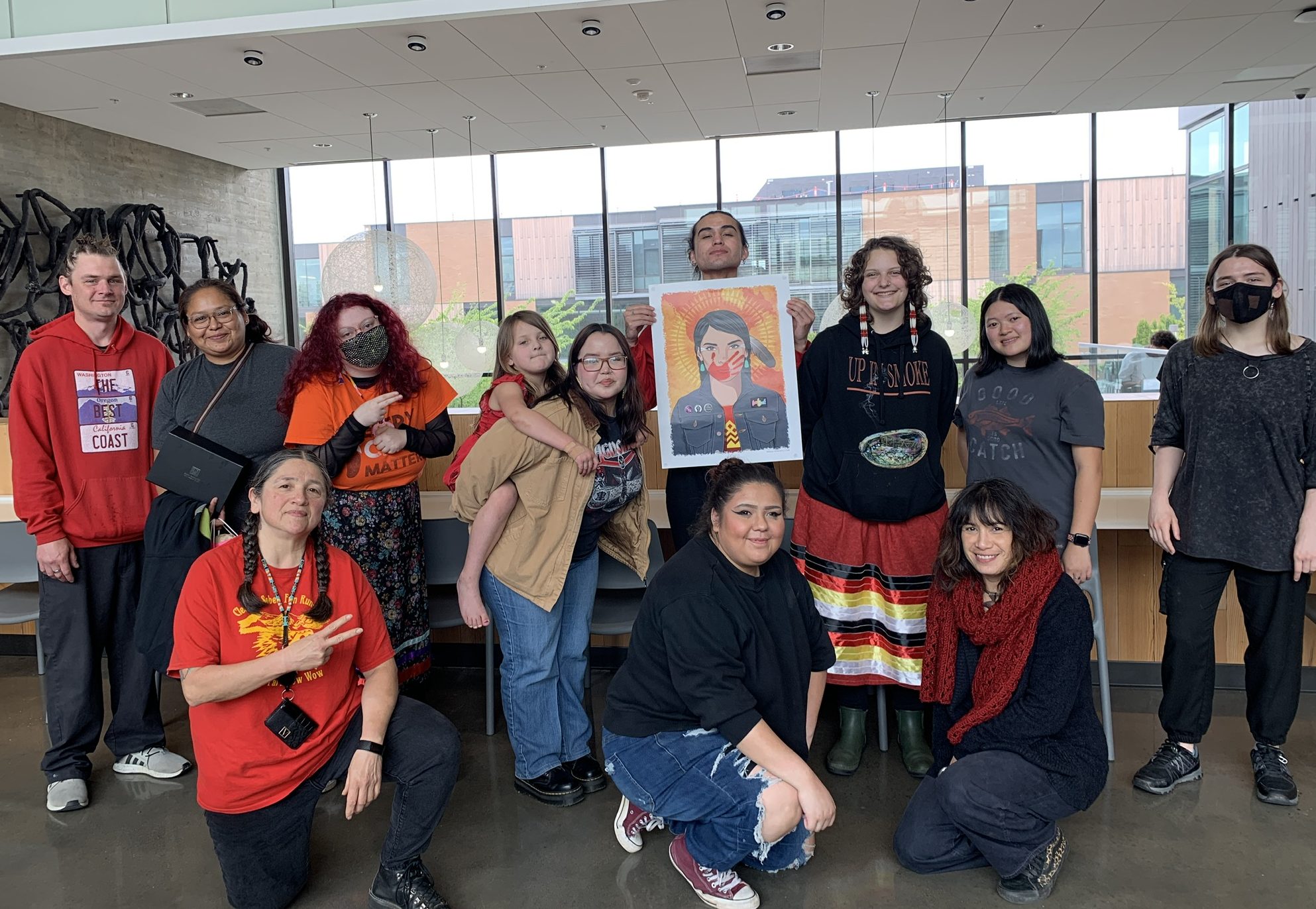 group of students kneeling and standing. A student is holding a poster of a women with a red painted hand over her mouth