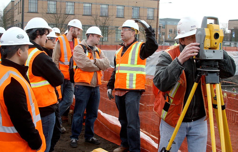 Derrick Beneville, project manager for Hoffman, discusses with the PCC students the kinds of jobs that are on the Cascade construction site. On the right, surveyor Darryl Ming of Ming Surveyors, Inc., scopes out the area.