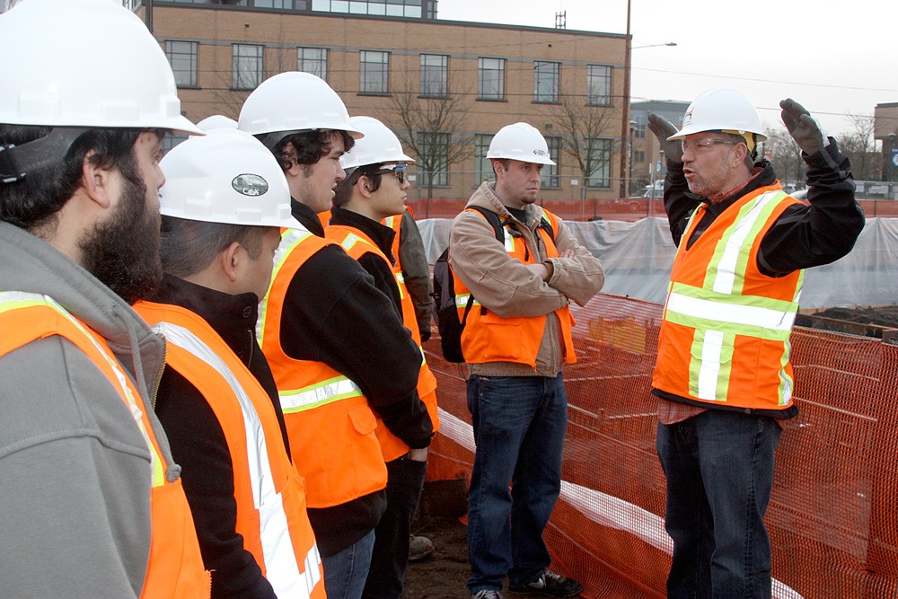 Derrick Beneville, project manager for Hoffman, discusses with the PCC students the kinds of jobs that are on the Cascade construction site. On the right, surveyor Darryl Ming of Ming Surveyors, Inc., scopes out the area.