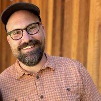 Bearded man wearing glasses and hat smiling