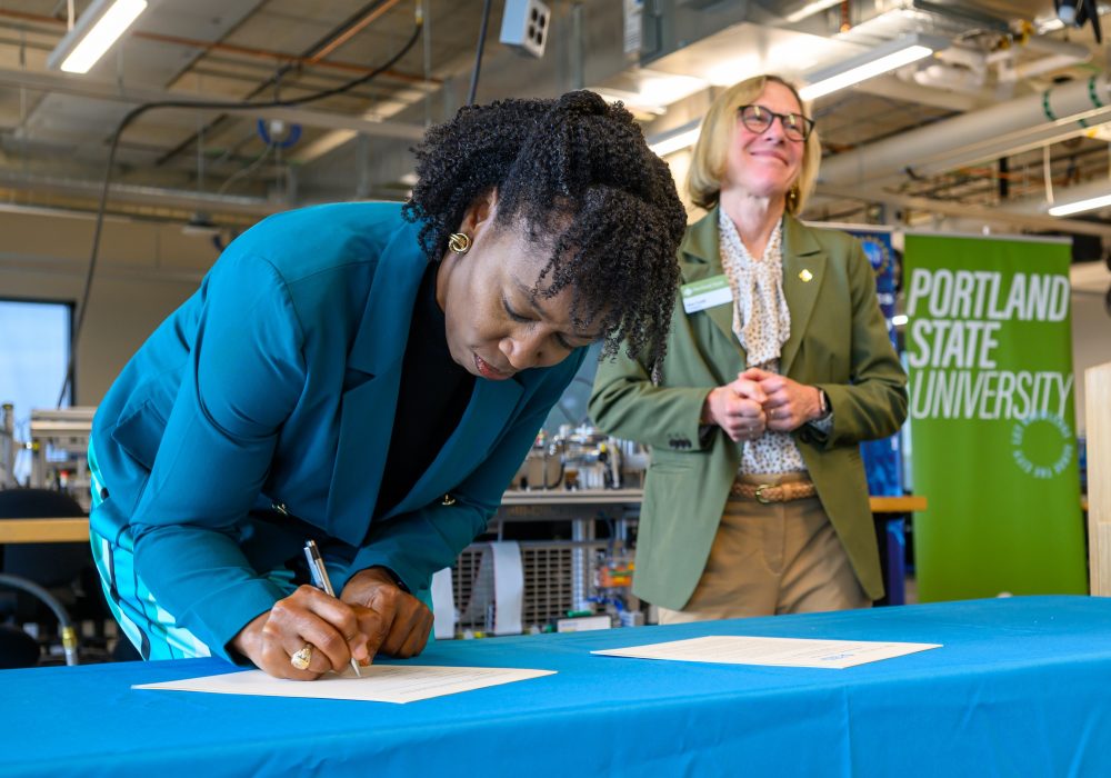 PCC President Adrien Bennings signs as PSU President Ann Cudd watches