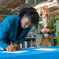 PCC President Adrien Bennings signs as PSU President Ann Cudd watches