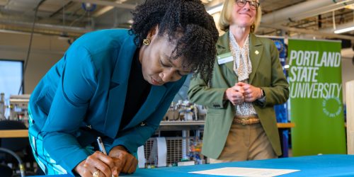 PCC President Adrien Bennings signs as PSU President Ann Cudd watches