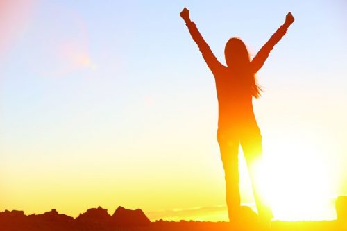 A woman with her arms up in victory after having reached the summit.