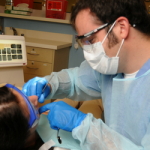 Male dental student works on a patient's teeth in a dental clinic setting.