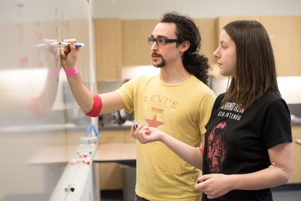 Two students write what they have learned on whiteboard in CLIMB classroom