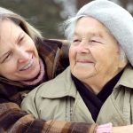 Aging adult mother looks up as she is hugged by her adult daughter