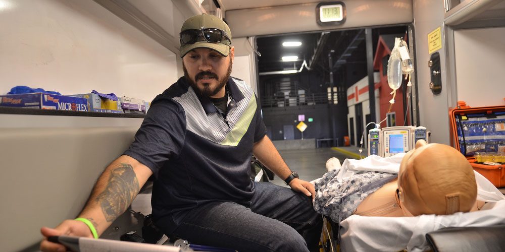 Young man practices emergency medicine and critical care techniques with life size medical dummy in ambulance training