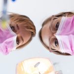 two dental assistants peering at a patient with tools in hand