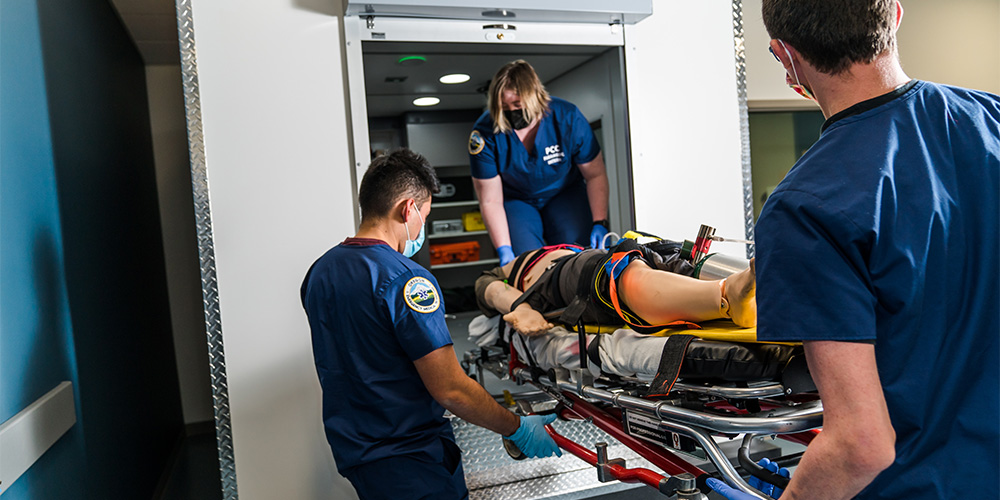 Students loading a dummy into a fake ambulance