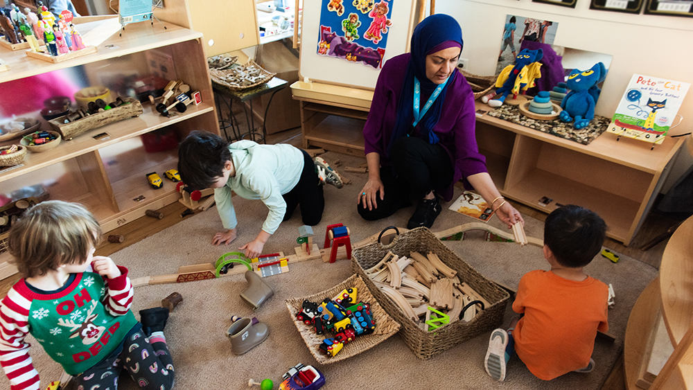 Teacher building train tracks with preschool students