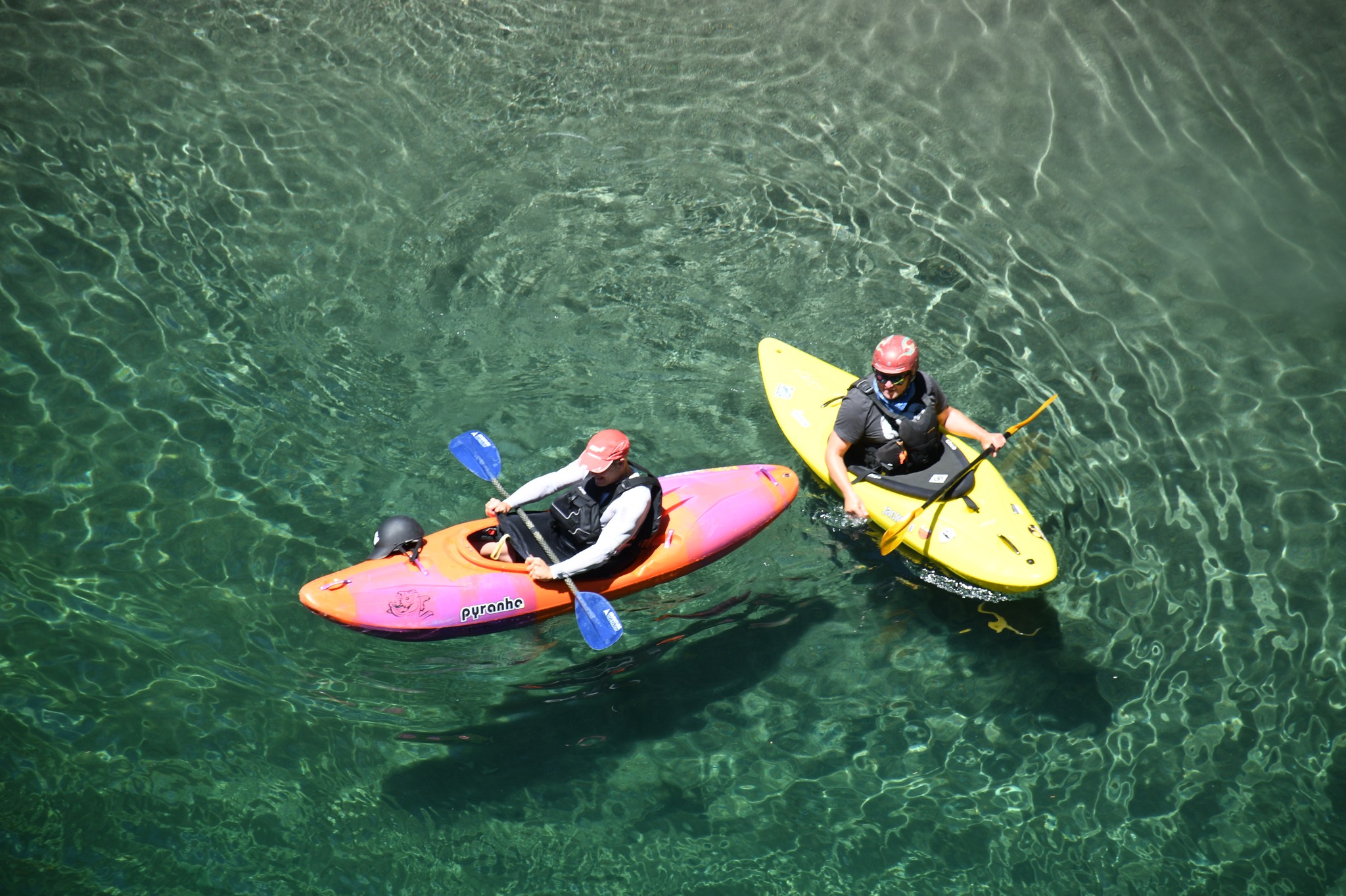 A picture of the instructor and a friend in hardshell kayaks on the Smith River near the Oregon and California border. The water of the Smith River in the summer is crystal clear and the picture was taken by a friend standing on a small bridge over the river.