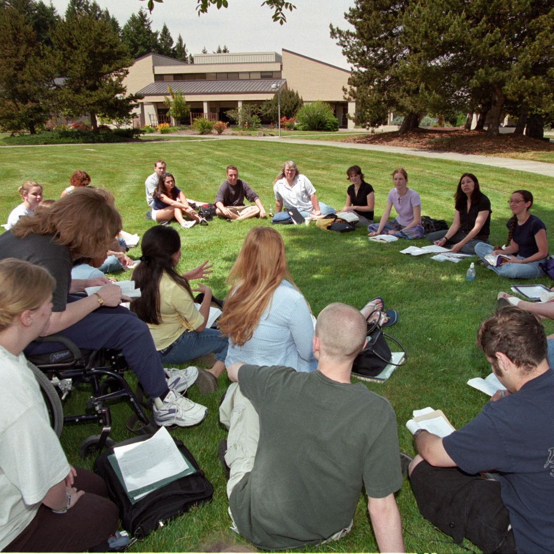 group of students sitting in a circle on a campus lawn