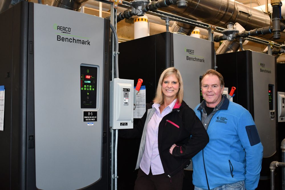 A woman and man pose in front of a boiler.